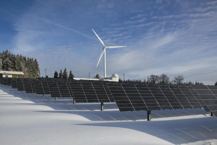 Solar panels in a snow-filled field and a windmill in the distance.